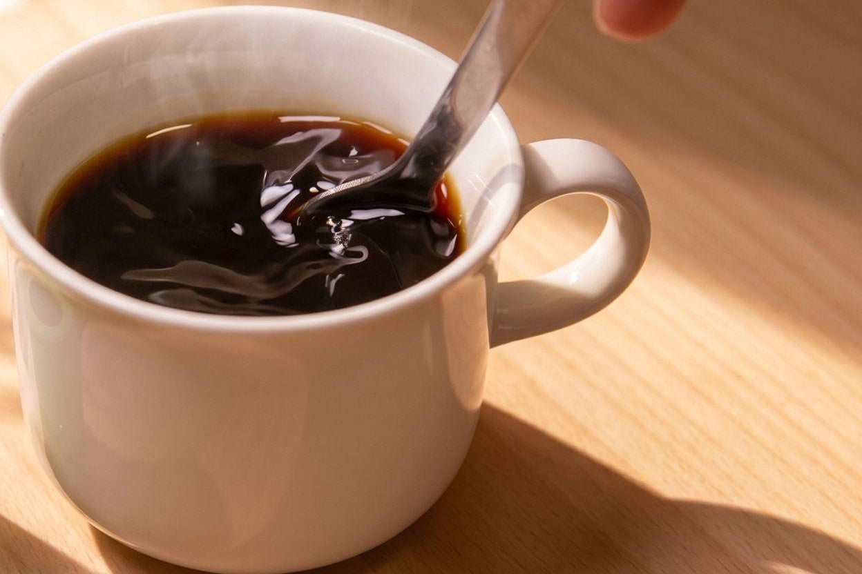 マグのコーヒーを、スプーンで混ぜる